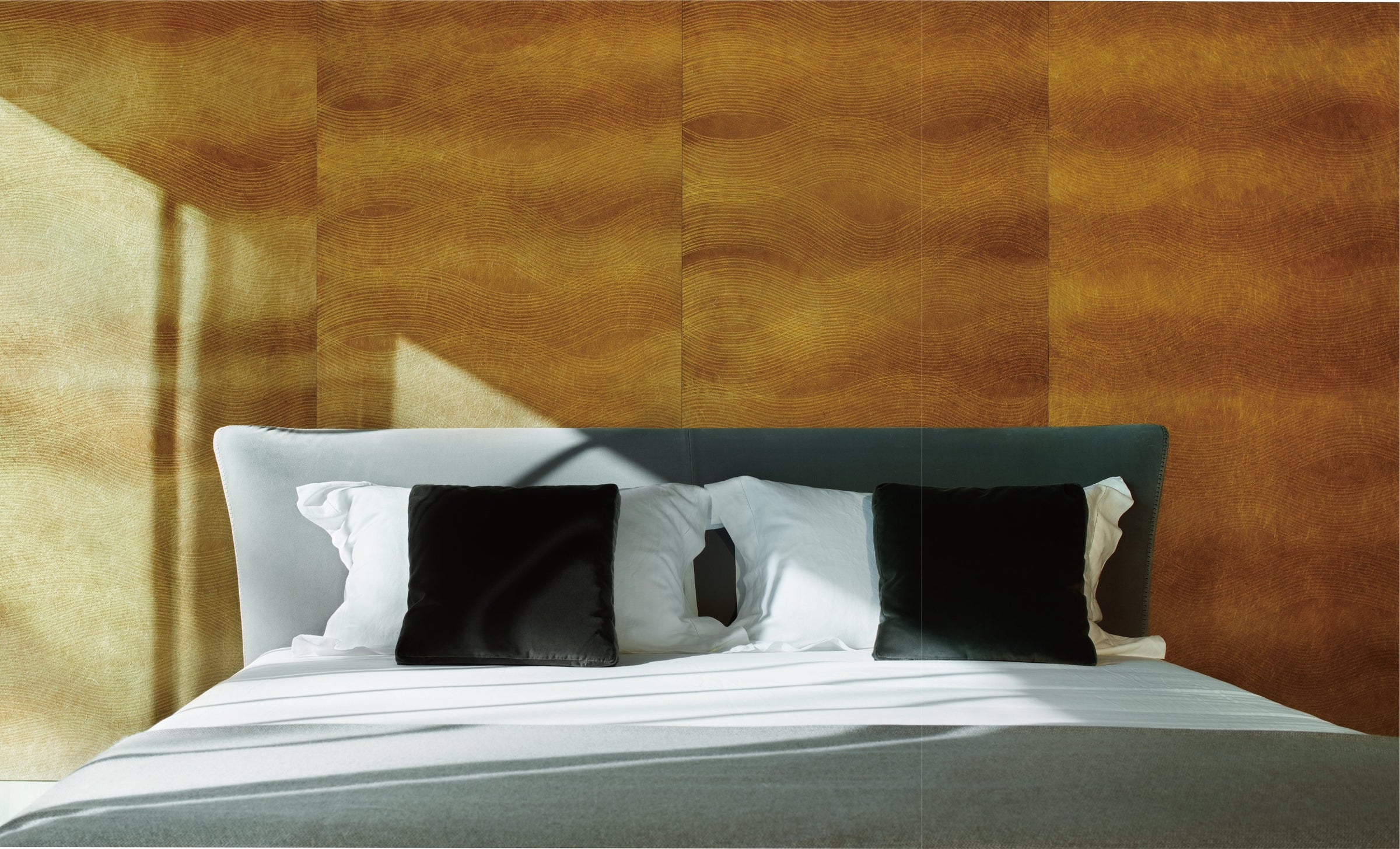 Bedroom with a gold leaf wallcovering behind the bed, sunlight falling across the wall