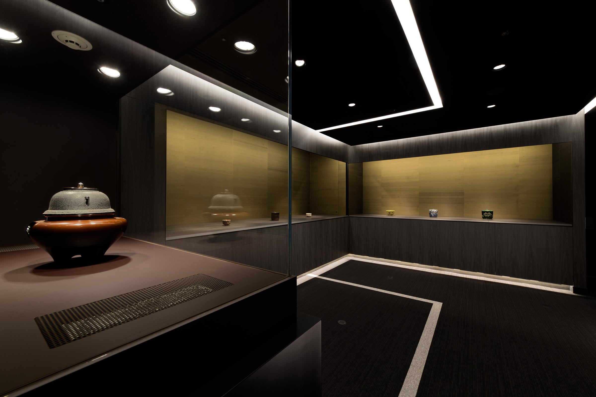 Gallery with lit display niches lined in Joan Silk, dark walls and a bronze vessel in the foreground