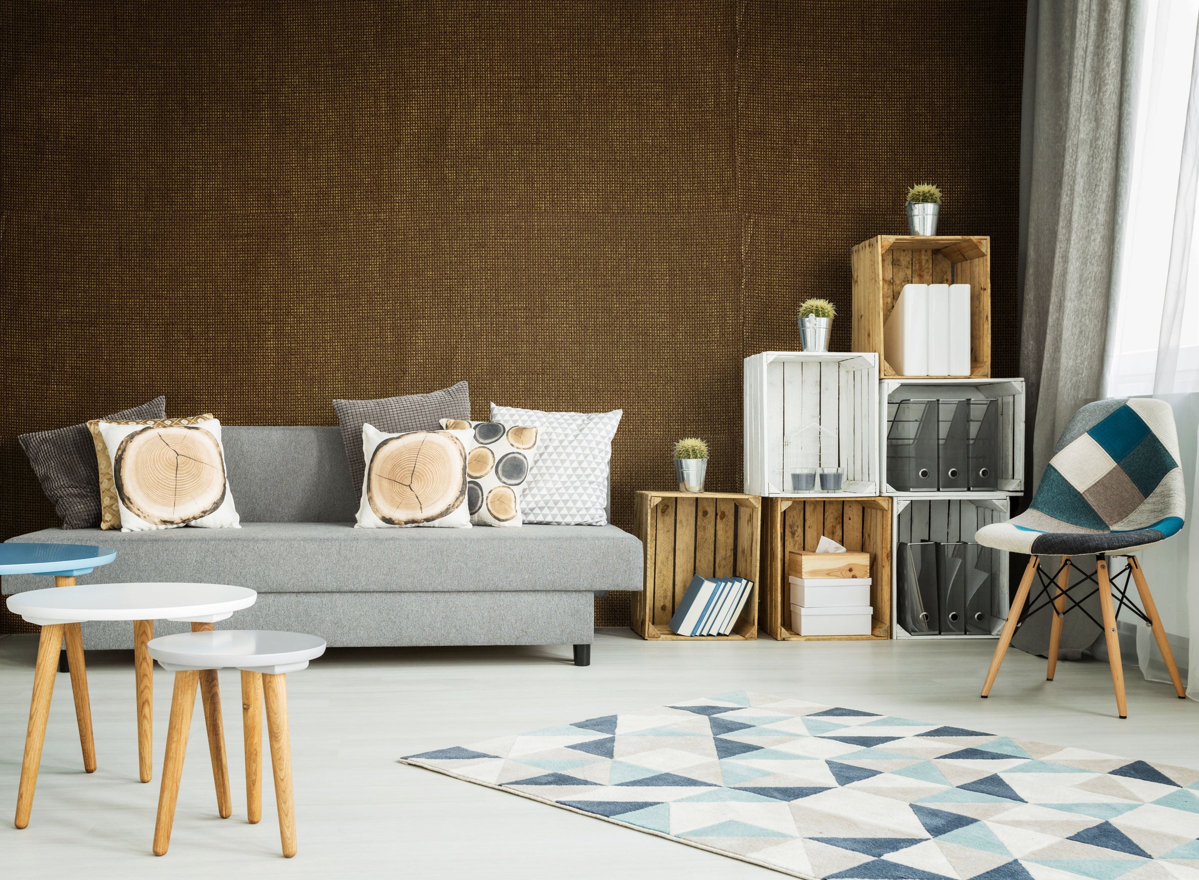 Living room with a deep brown woven wallcovering behind a grey sofa, wooden crates and a patchwork chair