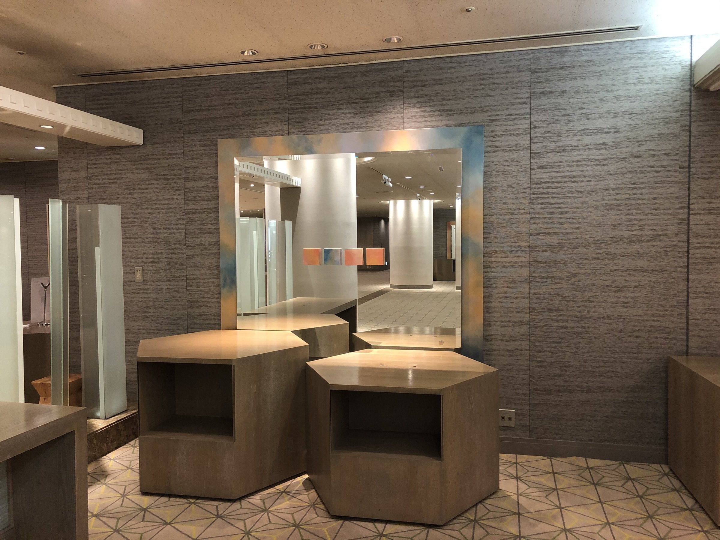 Grey textured wallcovering in panels across a hotel lobby, with wood display units and a large mirror