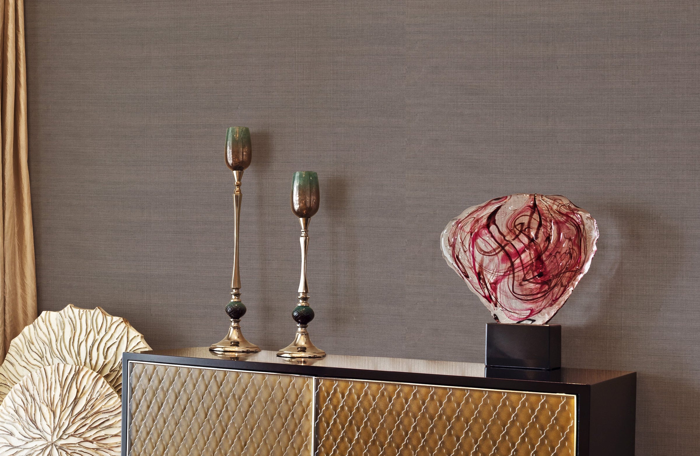 Taupe natural-weave wallcovering behind a black and gold cabinet with brass candlesticks and a glass sculpture